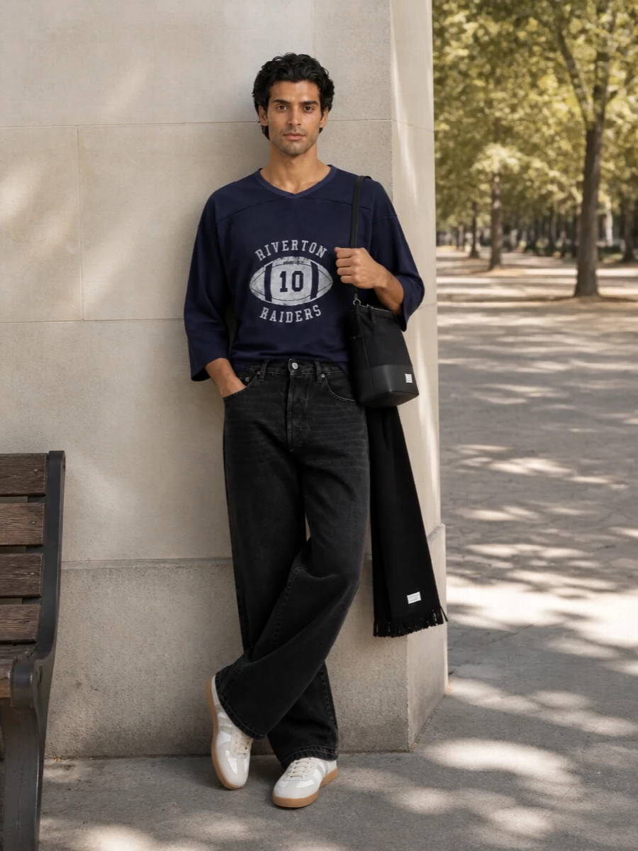 Navy collegiate jersey, washed black wide denim and off-white gum-sole sneakers create a studied mix of sport and grunge that still reads precise. The volumes stay relaxed on top and bottom, while the structured Margiela shoulder bag and inky scarf sharpen the mood just enough for city days and low-key evenings. It feels like classic campus energy, translated into grown-up, quiet luxury streetwear.