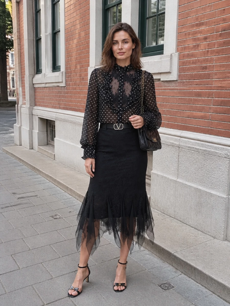 This look leans into dark romance: the sheer polka-dot blouse and black lace midi skirt create a long, fluttering silhouette that feels precise yet softly seductive. Nude-blush and black stilettos keep the leg line clean, while a quilted black shoulder bag and crystal-detailed belt introduce just enough gold and sparkle to underscore the blouse’s couture-level detailing. It’s an elegant SS cocktail outfit that reads impeccably polished and unmistakably Valentino Garavani.