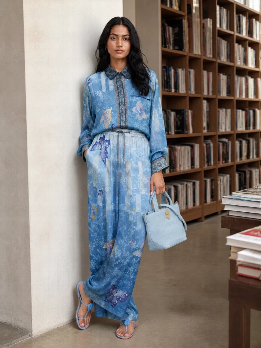 A poetic head-to-toe Pierre Louise Mascia set, the ombré butterfly shirt and wide-leg trouser read like a single, flowing artwork in layered shades of blue. Powder-blue lace-up sandals keep everything light and romantic, while a sculpted suede tote in the same cool tone grounds the print story with quiet structure. An optional gauzy scarf in matching sky-to-ice hues adds a final, whisper-soft note for cooler evenings or travel days.