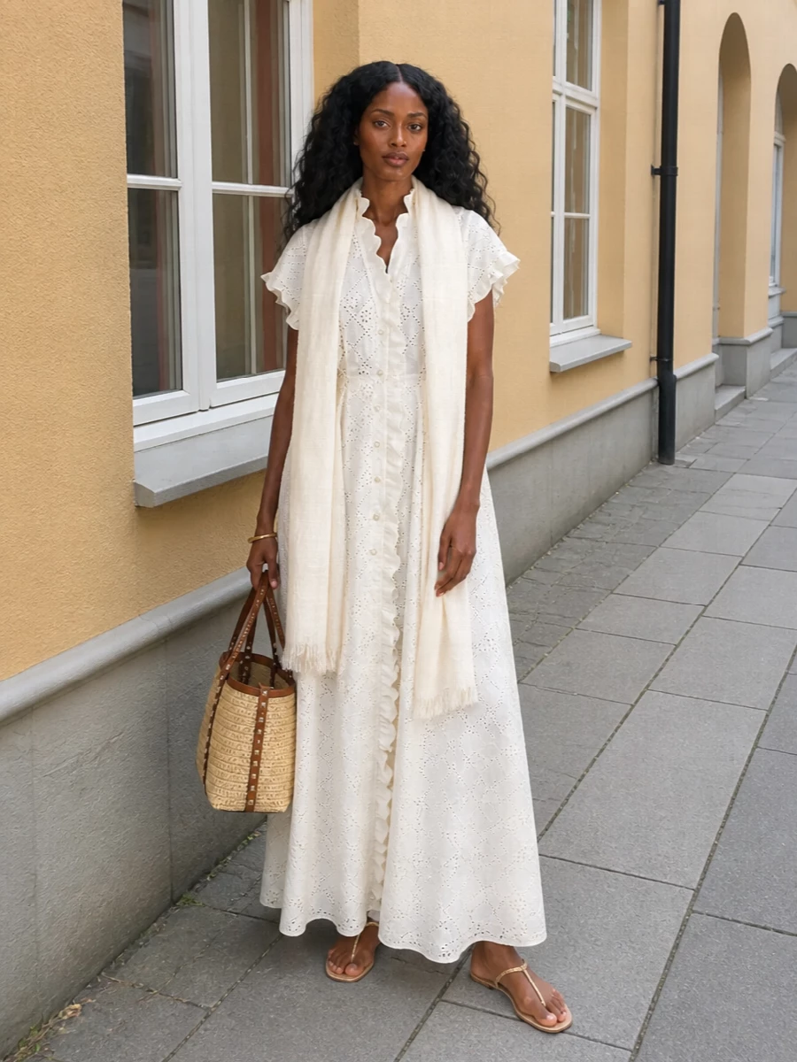 An ivory-on-ivory story that keeps the Alberta Ferretti dress light, romantic and quietly polished. Barely-there champagne sandals and a structured straw Valentino tote ground the broderie, while a single gold cuff and gauzy stole add just enough sheen and softness for garden lunches or seaside terraces. The result is airy and feminine, with texture and detail doing the work instead of loud color.