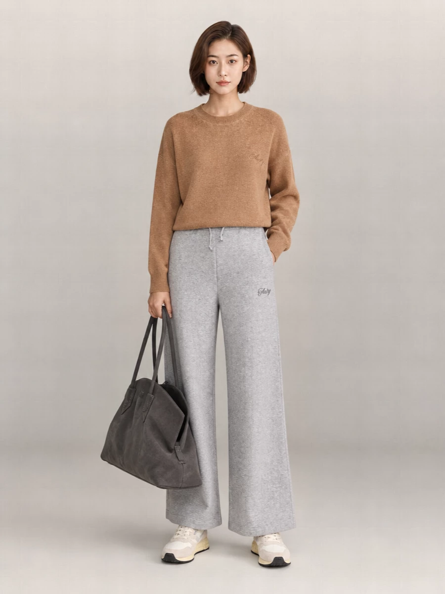 A soft camel knit with heather grey wide-leg jersey leans into relaxed, quietly sporty ease. Cream and beige runners keep everything light at the base, while a charcoal suede tote adds structure and texture. The neutral palette feels calm yet intentional, ideal for travel days or slow city weekends.