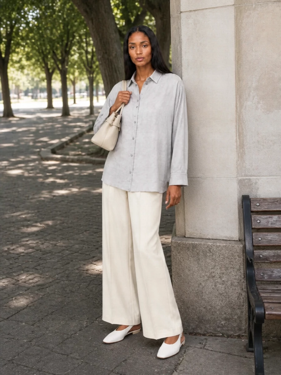 Soft grey and buttercream tailoring come together in an easy column that feels relaxed yet decidedly polished. The longline shirt and wide-leg trouser create a fluid, lengthening line, grounded by a flat slingback and a structured ivory top-handle for quiet day-to-dinner ease.