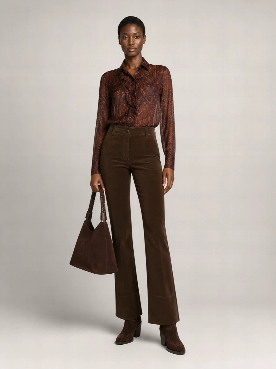 This outfit leans into a rich, boho interpretation of Western city dressing: the sheer paisley shirt and deep chocolate flared trousers create a long, fluid column for the sculpted boots to ground. Choosing the top and trouser path over a dress keeps the proportions sleek and versatile, ideal for anything from gallery afternoons to intimate dinners. The suede tote quietly repeats the textures and tones, so the whole ensemble reads considered but relaxed rather than costume Western.