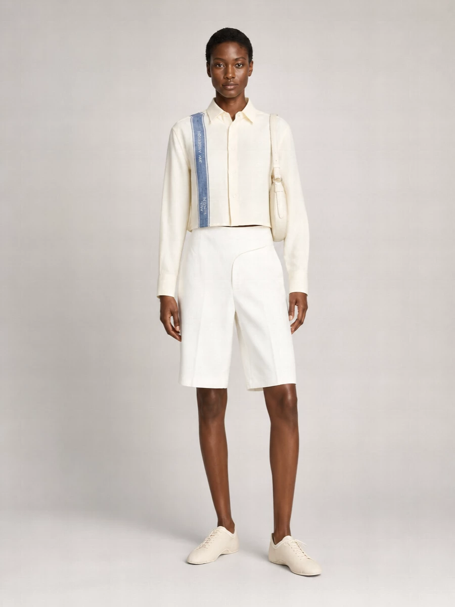 Buttercream shirting and precise white tailoring set a calm, quietly confident base, with the knee-length short keeping the proportion modern and city-ready. Bare, minimal cream lace-ups and a sculpted ivory shoulder bag keep the palette soft and the attitude low-key, so the graphic stripe detail feels considered rather than loud.