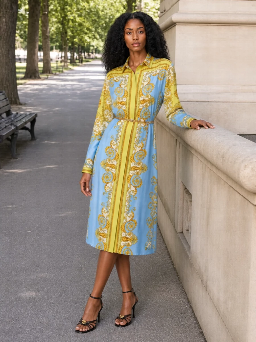 A baroque shirt dress in powder blue and citrus stays front and center, cinched with a gleaming chain belt that mirrors its gold scrollwork. Black and gold strappy sandals and a structured top-handle bag sharpen the romance into something city-cocktail ready while keeping the palette clean and cohesive. The result is polished, summery and confidently Versace without feeling over-styled.