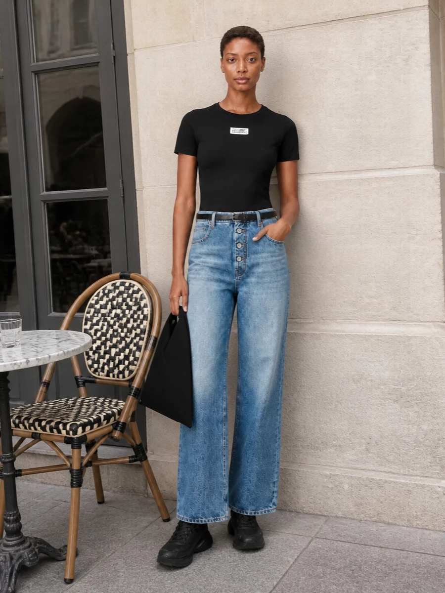 A black logo tee meets high-rise wide-leg denim for a clean Margiela take on everyday streetwear. Chunky black runners keep the palette tight and practical, while the origami tote and slim belt add just enough structure. It reads graphic and low-key, with the proportions doing the work rather than overt styling tricks.