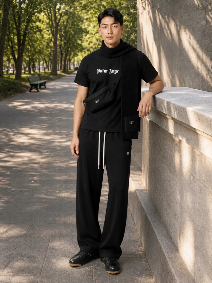 A clean Palm Angels tee sits over relaxed wide-leg track pants for a low-slung, LA-skate silhouette in strict monochrome. Black Prada sneakers sharpen the base, while the nylon crossbody and ribbed scarf add just enough technical detail to keep the outfit polished without breaking its street energy.