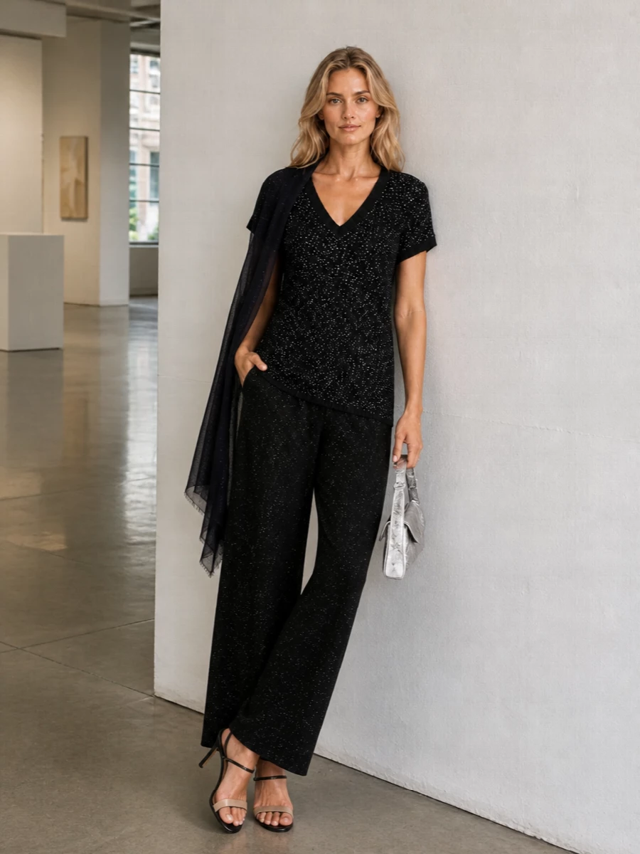 A long, shimmering black knit meets fluid wide-leg trousers for a clean evening column that reads relaxed yet intentional. Strappy black heels and a sculptural silver baguette underline the quiet glamour, while a gauzy midnight wrap adds an extra veil of light for terrace dinners and late bar stops.