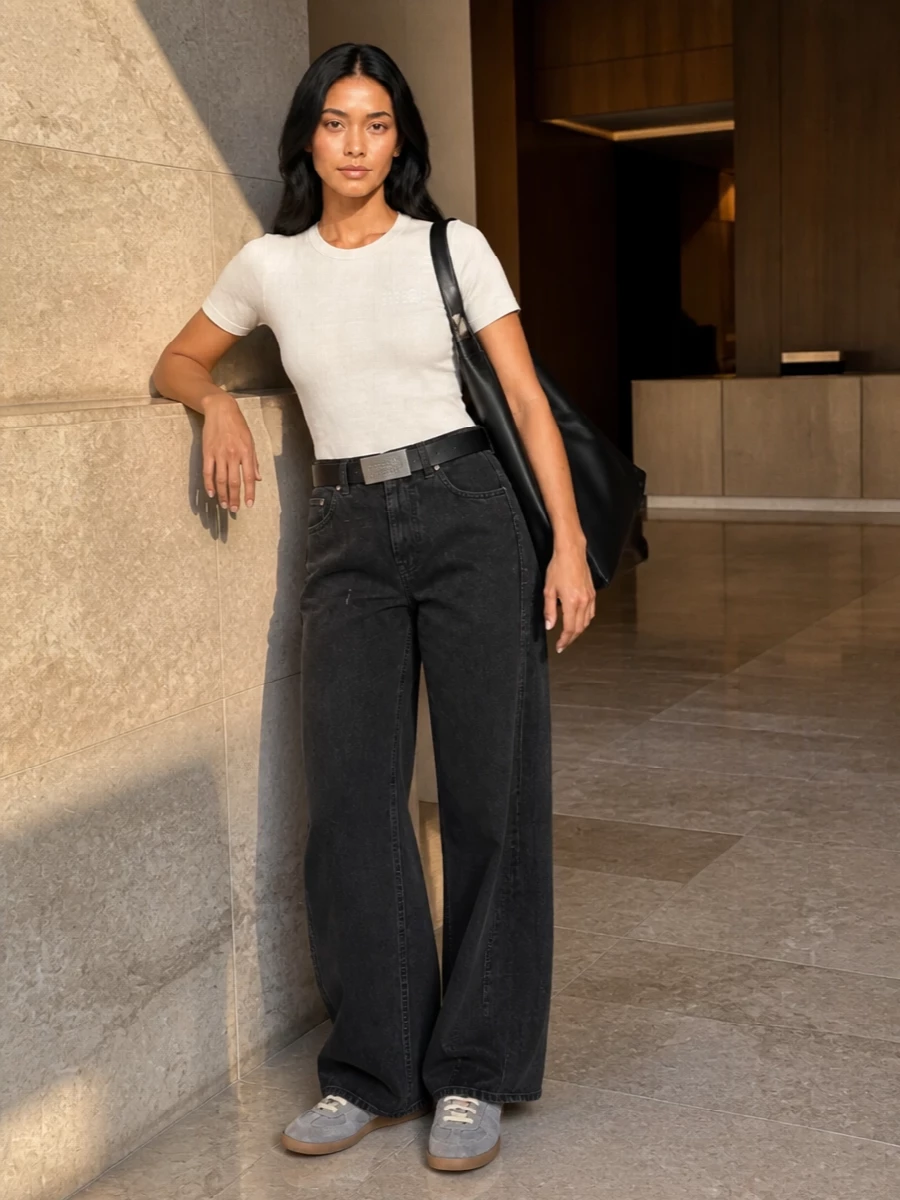 A light-beige Margiela tee sits against washed-black wide-leg denim for a clean, graphic contrast that still feels easy. Grey-and-cream sneakers and the black Japanese tote keep everything in a tight, minimal streetwear palette. The numeric-logo belt quietly sharpens the waist so the wide leg reads intentional, not slouchy.