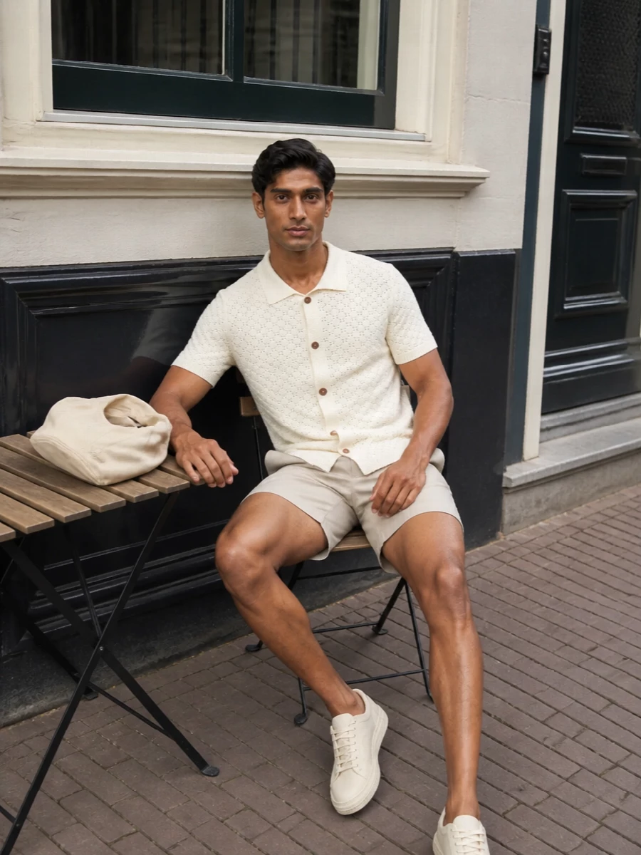 A soft, tonal take on summer ease, this pairing keeps everything in the off‑white and light‑beige family so the texture of the knit does the talking. The tailored‑sport short and clean leather sneakers keep it polished enough for city days while still feeling relaxed. A compact neutral tote finishes things with a subtle design twist rather than a loud logo moment.