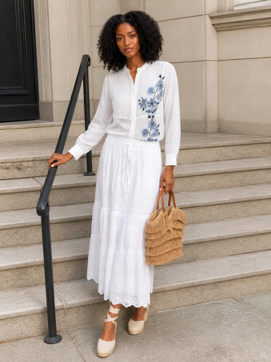 A soft white story with touches of dusty blue keeps this outfit romantic and sunlit, perfect for garden parties or long coastal lunches. The sheer embroidered shirt brings quiet structure against the float of the tiered maxi, while the ivory espadrille wedges and raffia tote ground everything in an easy Mediterranean mood. It feels feminine and relaxed yet still considered enough for warm-weather celebrations.