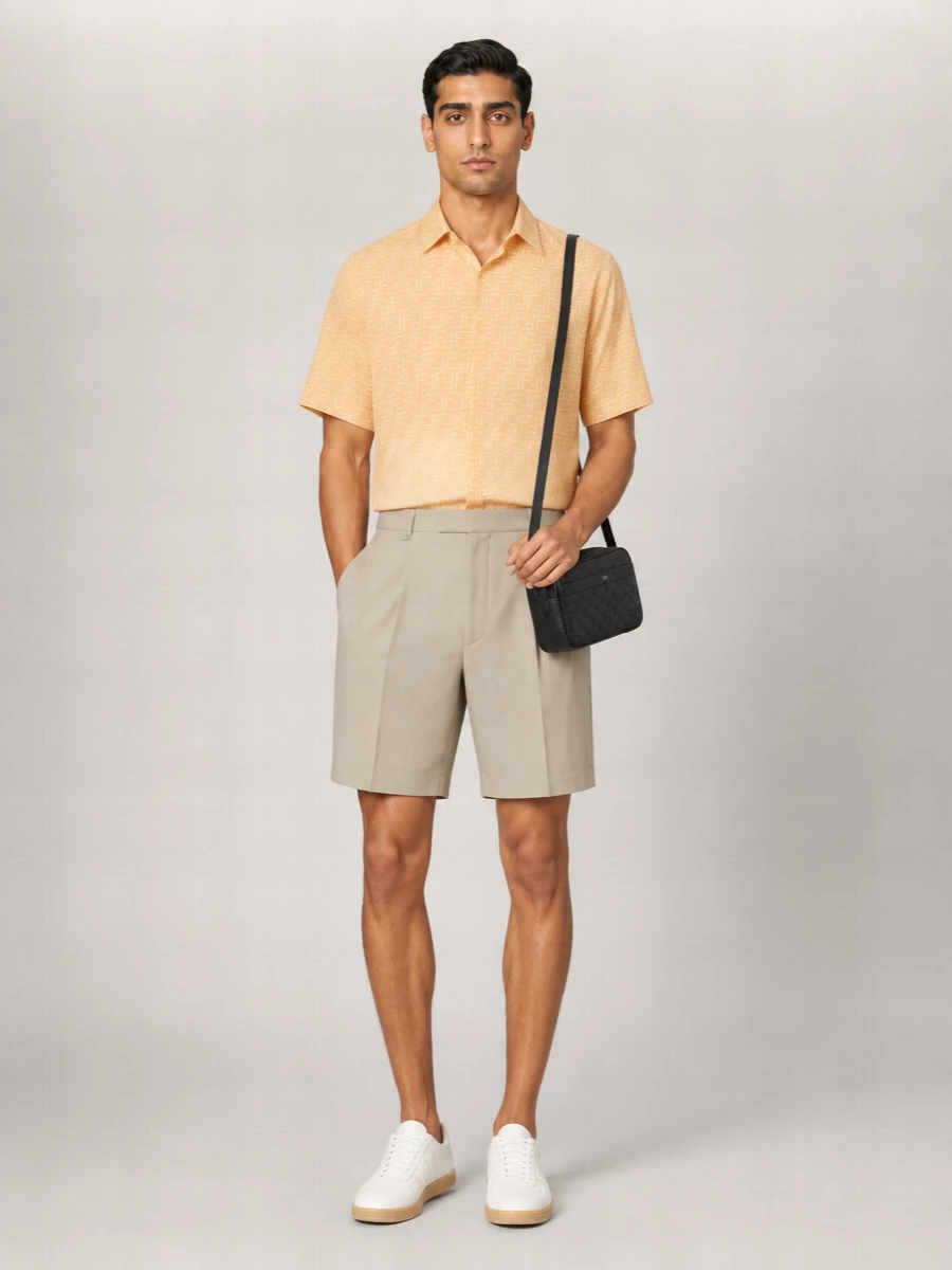Soft amber against stone beige creates a calm, sun-lit palette that reads considered without feeling formal. The high-rise pleated short and clean sneakers keep the proportions sharp but relaxed, ideal for warm city days or coastal weekends. A structured black crossbody adds just enough precision to ground the ease of the tailoring.