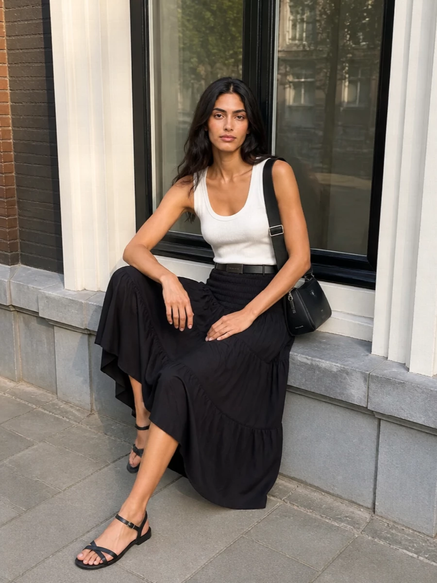 A clean black and white palette keeps this tiered midi grounded, pairing a soft ribbed tank with barely-there sandals for warm days in the city. The scooped neckline and smocked waist balance volume and definition, while a structured belt and sleek cross-body add just enough polish for dinners after errands.