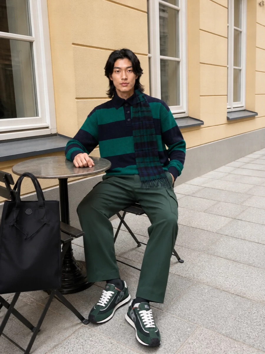 Navy and forest sit in the same register from knit to cargos and sneakers, so the colour story feels deliberate rather than matchy. The straight leg and low‑profile runners keep the rugby polo relaxed but not sloppy, with a clean black tote and subtle tartan scarf adding a city‑ready finish. It is an easy weekend uniform that can move from coffee to casual dinner without needing a change of pieces.