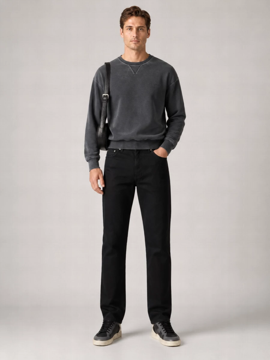 A washed charcoal sweatshirt sits over inky straight-leg denim for a monochrome base that feels calm, graphic and quietly assertive. Black skate-inspired sneakers and a sculpted shoulder bag keep the energy street-led but polished, with subtle texture doing the work instead of logos or color. The result is a low-key uniform that feels as considered for city evenings as it does for slow weekend days.