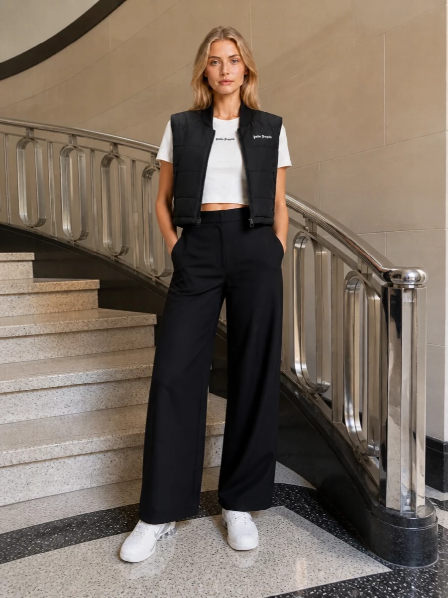 I’m building around the Palm Angels gilet as a cropped, technical shell, so separates win over a dress for cleaner layering and better proportion control. The off-white cropped tee and high-waisted wide-leg trousers give a sharp black-and-cream base that feels modern and minimal, while the sleek Nike sneakers and quilted Moncler tote keep everything in a light, athletic streetwear register. The result is a monochrome, logo-threaded Palm Angels-centric outfit that feels relaxed but intentional for cool city days and travel.
