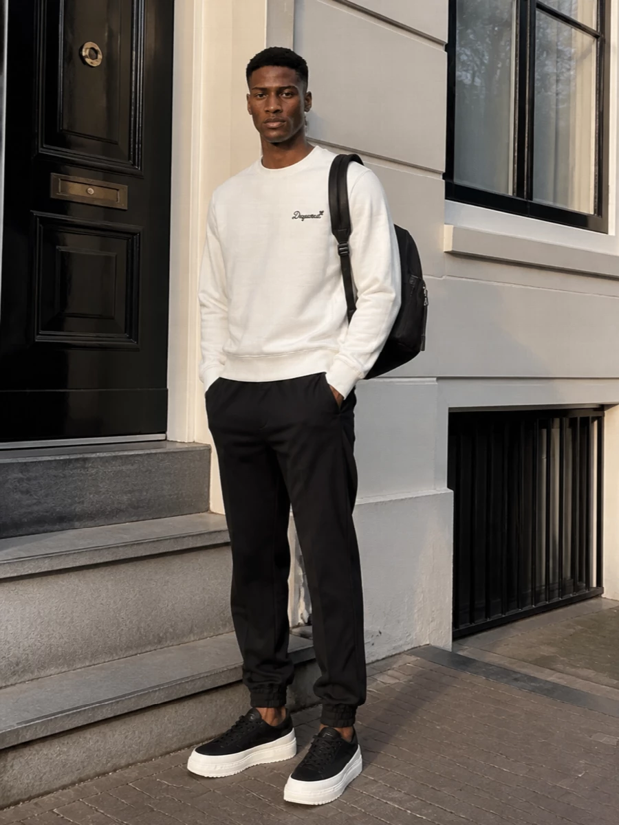 A clean monochrome story built around the Moncler sneakers, this pairing leans into soft off‑white and deep black for a sharp city mood. The collegiate crew and tailored joggers keep the silhouette relaxed but refined, letting the chunky sole be the graphic punctuation. A streamlined backpack finishes it with low‑key utility that still reads luxury street.