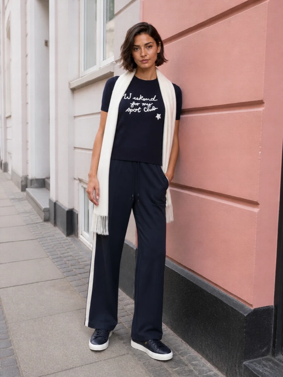 A navy-on-navy base keeps the graphic sport-club embroidery feeling grown up rather than playful. Wide-leg track trousers echo the tee’s athletic note, while refined navy sneakers and a structured tote keep it city ready. The ivory scarf quietly ties back to the embroidery, adding a soft highlight against the saturated blue.