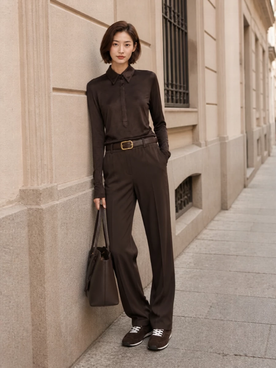 Rich coffee and chocolate tones keep this track pant pairing firmly in the Tom Ford universe, reading polished rather than sporty. The sheer shirt adds after-dark ease on top, while refined brown runners and a structured tote ground the outfit for city days that blur into dinner. A dark-chocolate belt quietly defines the waist so the relaxed silhouette still feels intentional and composed.