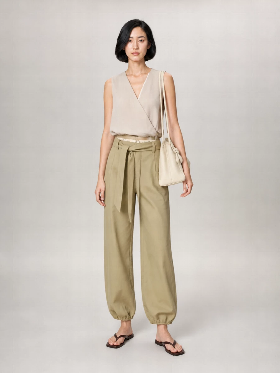 Soft neutrals and easy structure keep this pairing relaxed but considered, with the wrap tank echoing the trouser’s belt detail for a clean, cinched waist. Dark chocolate sandals ground the airy top and wide leg, while the buttercream tote keeps everything light and city ready. The result is a calm, utilitarian ensemble that moves from coffee runs to late afternoon plans without needing a change.