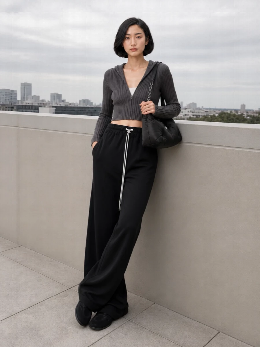 Charcoal ribbing meets inky, puddling volume for a long, grounded line under the cropped hoodie. The low-profile black sneaker keeps everything quiet and agile, while the padded hobo adds a tactile, downtown softness against the severe ribs and drawcords. It’s a city-uniform take on Rick’s off-duty mood, all about volume control in one restrained, monochrome palette.