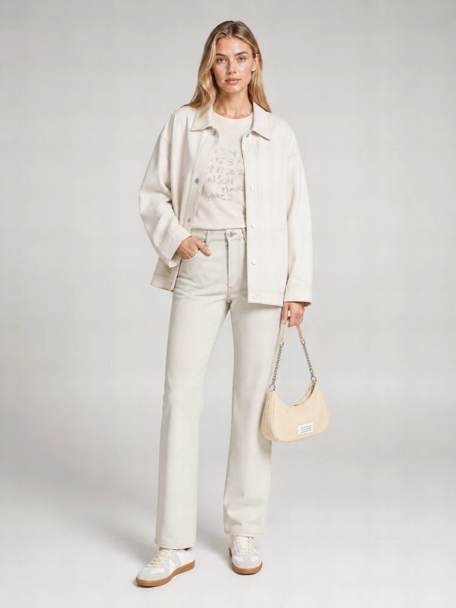 I am building around the coat as outerwear with a tee and denim rather than a dress, to keep its workwear-meets-gallery energy relaxed and street-informed. Pale stone jeans and an ivory Margiela numbers tee create a near-monochrome column under the off-white jacket, so all the interest sits in proportion and subtle stitching. Off-white low-top sneakers and a butter-beige crescent bag keep everything within the same soft-neutral family, landing in that sweet spot between minimalist daywear and quiet luxury uniform.