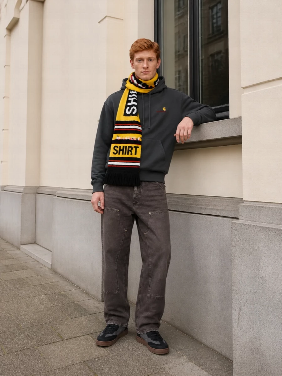 Carhartt WIP’s charcoal hoodie sits over relaxed tapered workwear denim for a grounded, skate-adjacent street uniform. Charcoal and black sneakers keep the palette tight, while a structured black tote and a hit of graphic scarf color make it city-ready rather than basic.