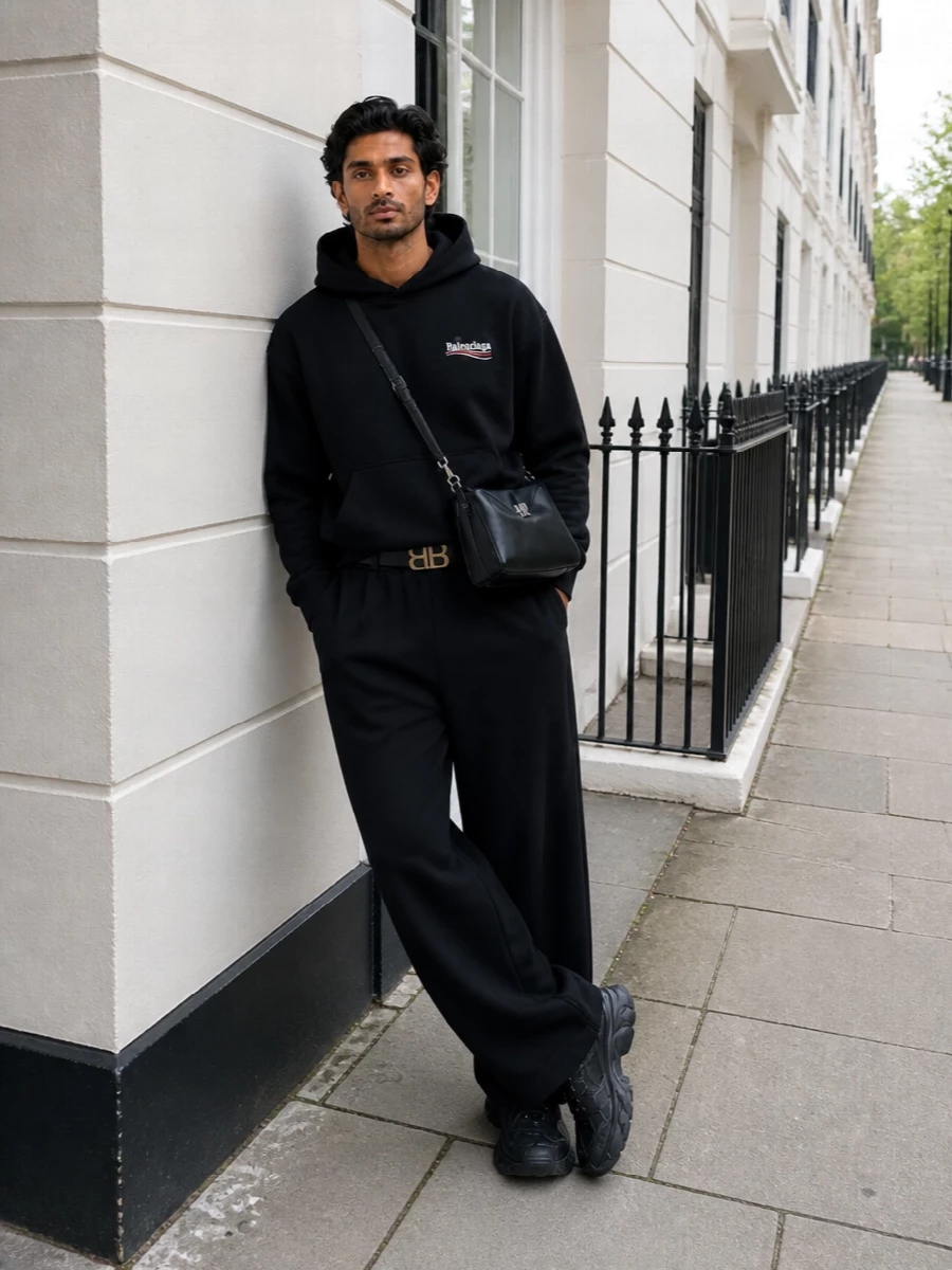 Balenciaga’s black logo hoodie sits over sweeping wide-leg trousers for a clean, monochrome take on streetwear volume. All-black technical runners echo the exaggerated proportions, while the structured crossbody and sculptural logo belt tighten the mood into something quietly assertive and city-ready.