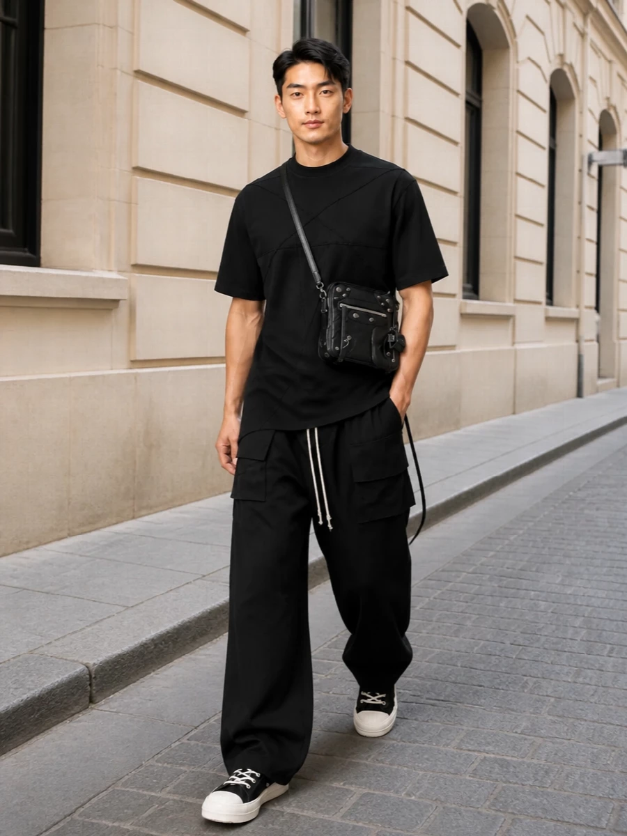 This look builds a stark, architectural Rick uniform: the longline harnessed tee flows straight into wide black cargo trousers, giving a clean, monolithic column. Chunky black hi-tops echo the graphic contrast at the hem, while the compact crossbody adds just enough hardware and attitude without disturbing the silhouette. The result is dark, directional streetwear that feels effortless but highly considered for SS layering.