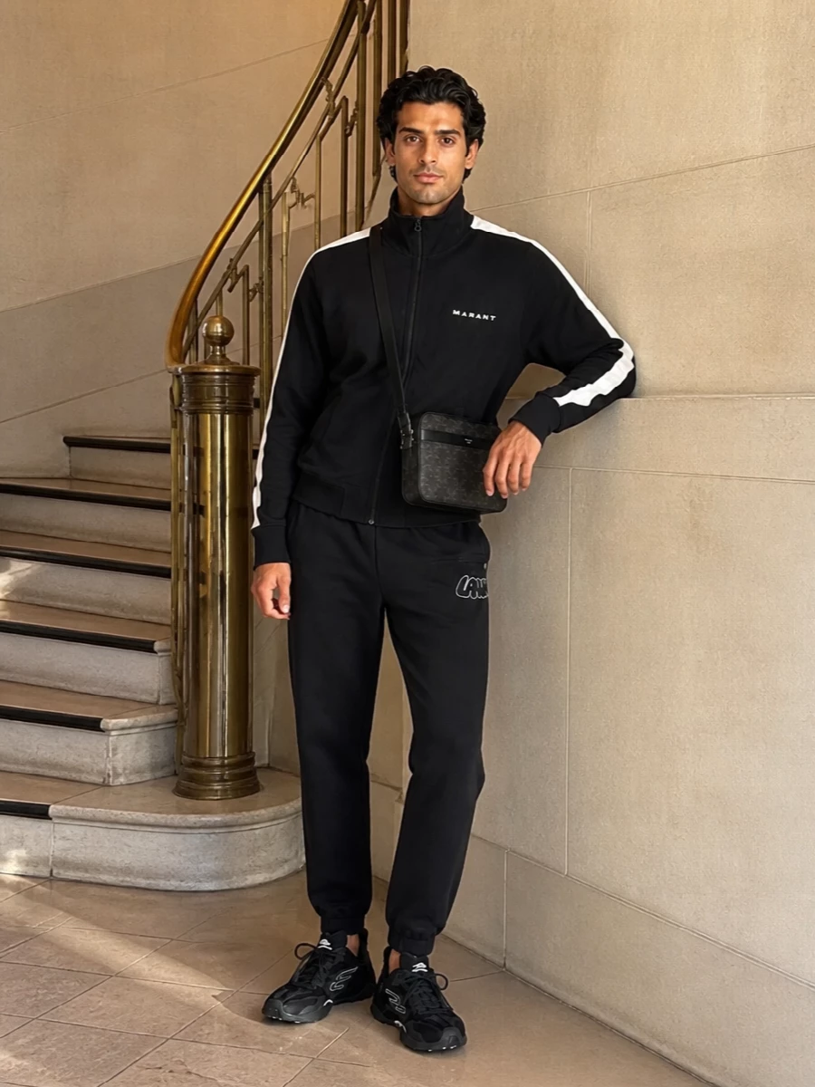 A monochrome, sport-led base keeps the focus on clean lines and the Balenciaga sneakers’ technical detail. The zip-front track top and tapered joggers create a streamlined, athletic silhouette that still feels refined. A compact logo crossbody adds just enough city polish without diluting the performance mood.