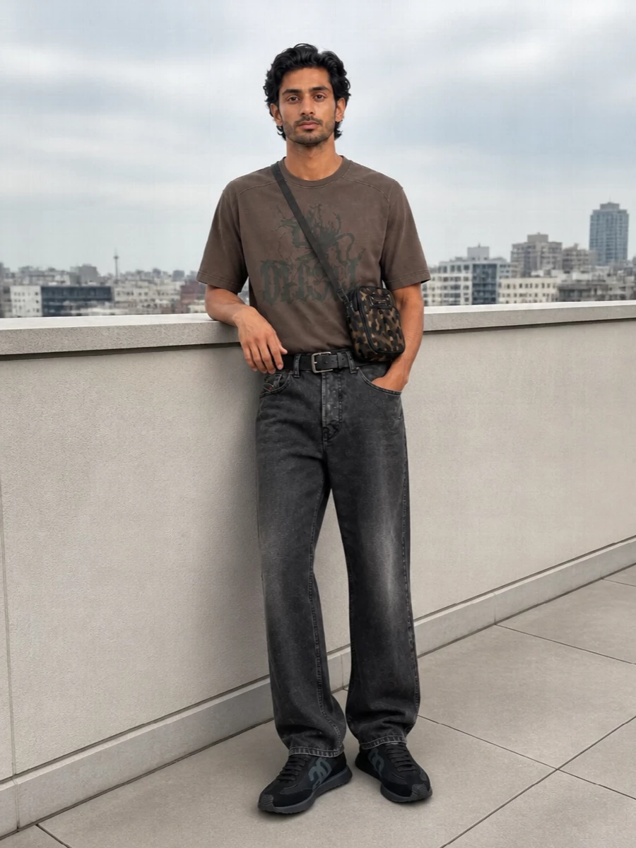 Washed brown and charcoal sit together for a dark, grunge‑leaning street outfit that still feels easy to wear day to night. The relaxed tee and straight denim keep the proportions unfussy, while the technical black runners and compact crossbody bring a sharper, city‑ready energy. Muted hardware and camo details echo the tee’s olive tone without competing with its graphic front.