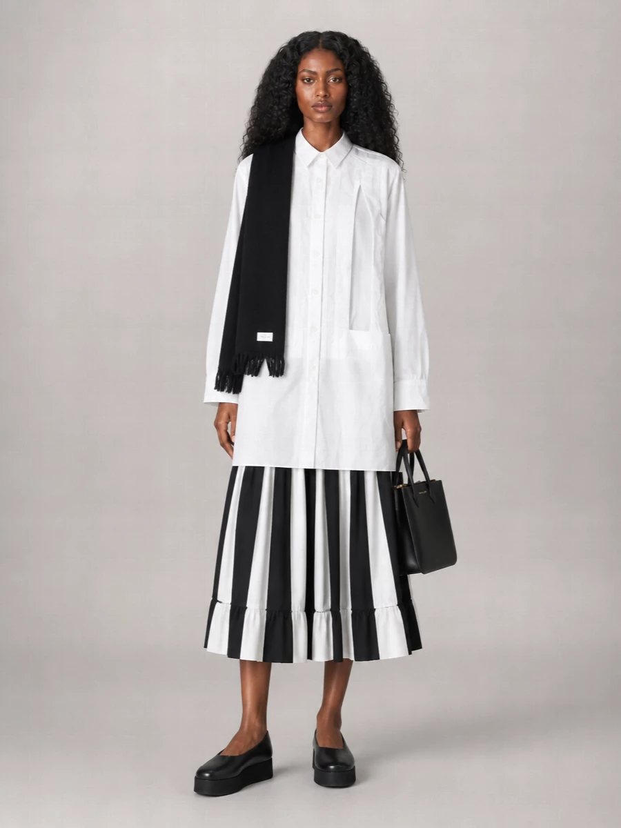 A graphic black and white story built around the full striped midi, this pairing leans into long, architectural lines with the extended Comme des Garçons shirt peeking beneath. Platform ballerinas and a sharp mini top-handle keep it grounded in the city, balancing art-school attitude with clean, wearable ease. The result is relaxed yet distinctly directional, ideal for days that move from errands to gallery visits without an outfit change.