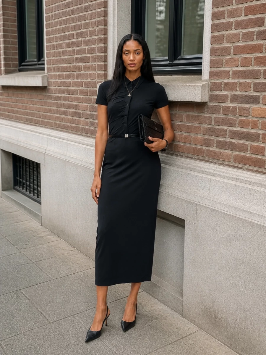 A sharply cut black shirt dress is cinched with a slim belt, then finished with pointed slingbacks and a structured clutch for a precise, after-dark silhouette. A fine orb pendant is the single glint of softness, keeping the mood controlled and quietly confident.
