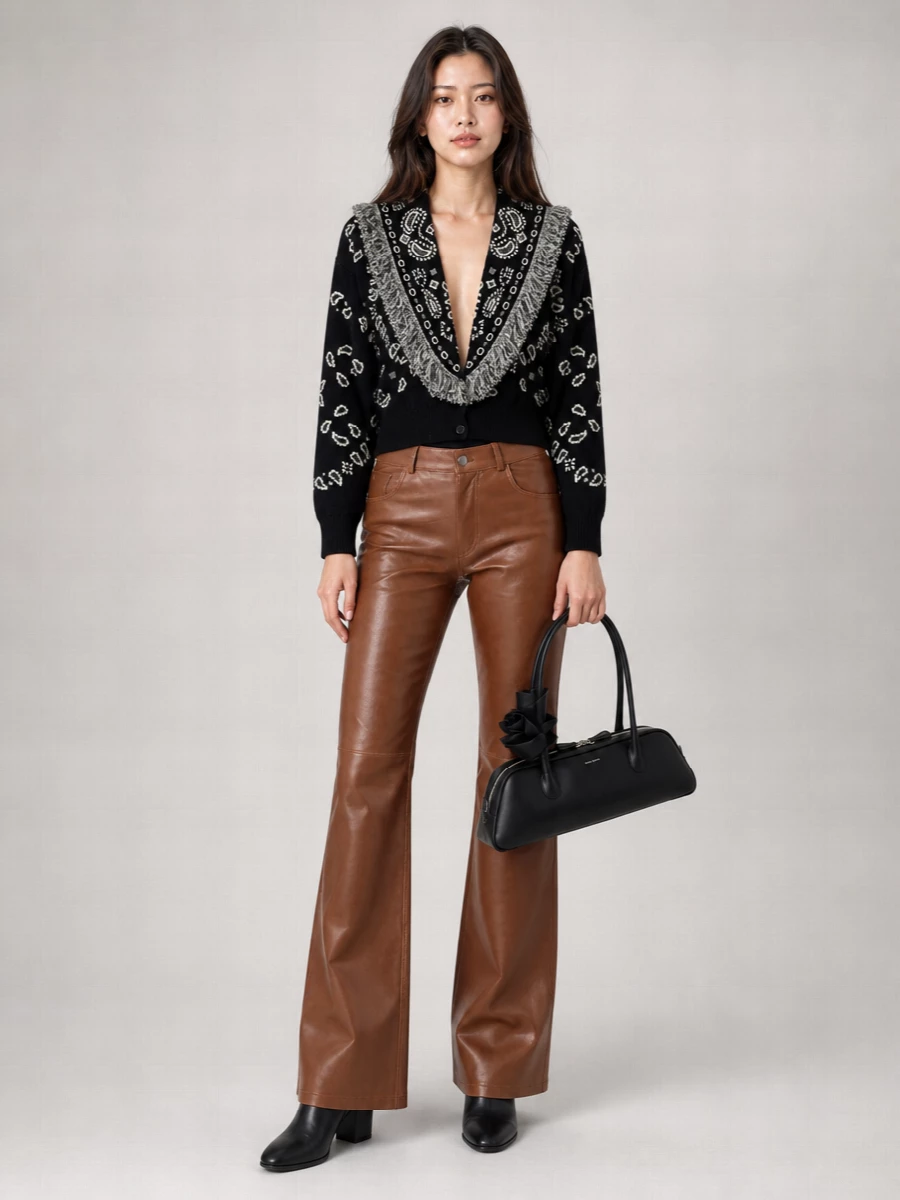 The bandana-fringed cardigan sits over caramel leather flares, giving a rich contrast of texture that still reads controlled and polished. Sleek black ankle boots lengthen the line, while the sculptural black shoulder bag quietly underlines the artistry. The result is a graphic, modern city outfit that moves easily from daytime errands to low-lit dinners without changing a piece.