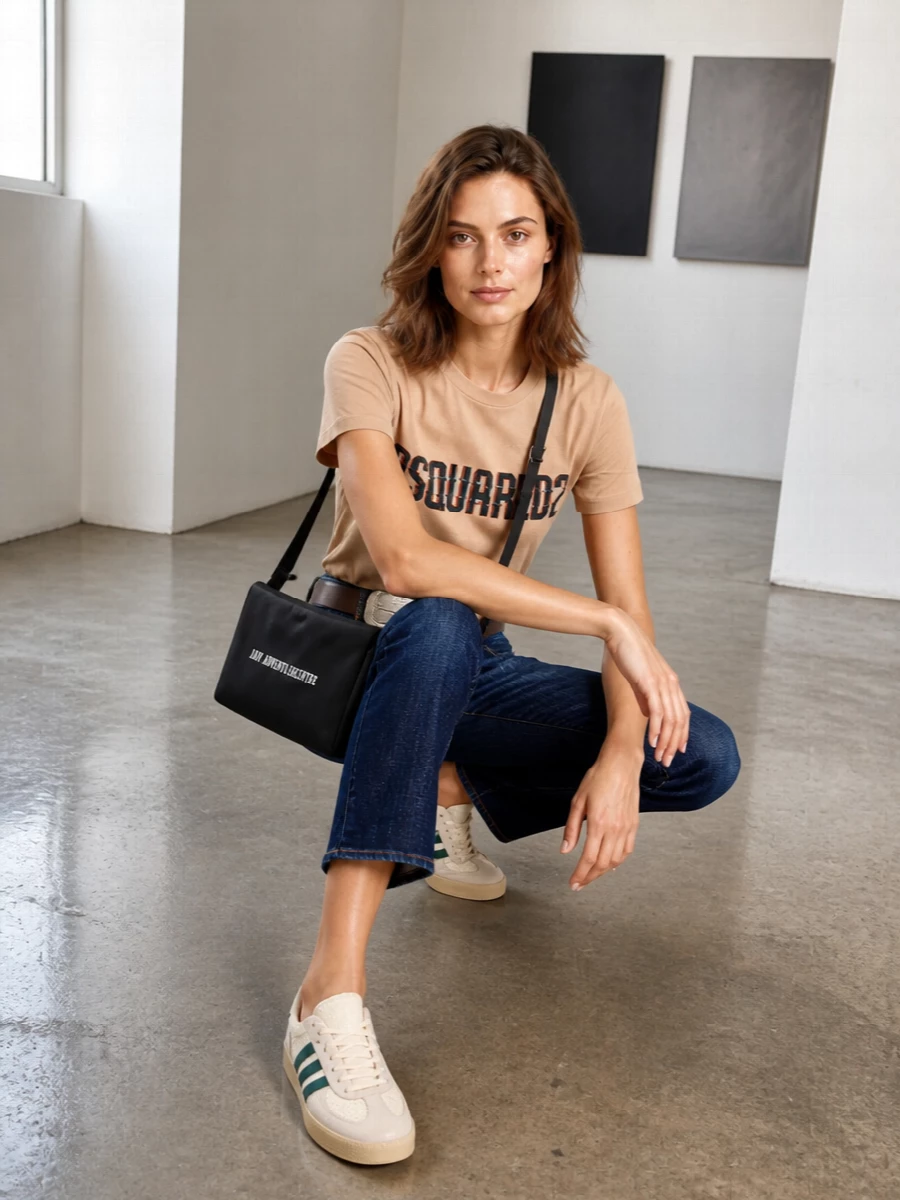 Peach logo jersey meets cropped, faded indigo denim for a street-preppy uniform that feels relaxed but considered. Cream and teal terrace sneakers echo the graphic lettering, while a black cross-body and Western-inflected belt add just enough attitude without crowding the palette. The result is an easy off-duty combination that still reads sharply styled from brunch to late-night walks home.