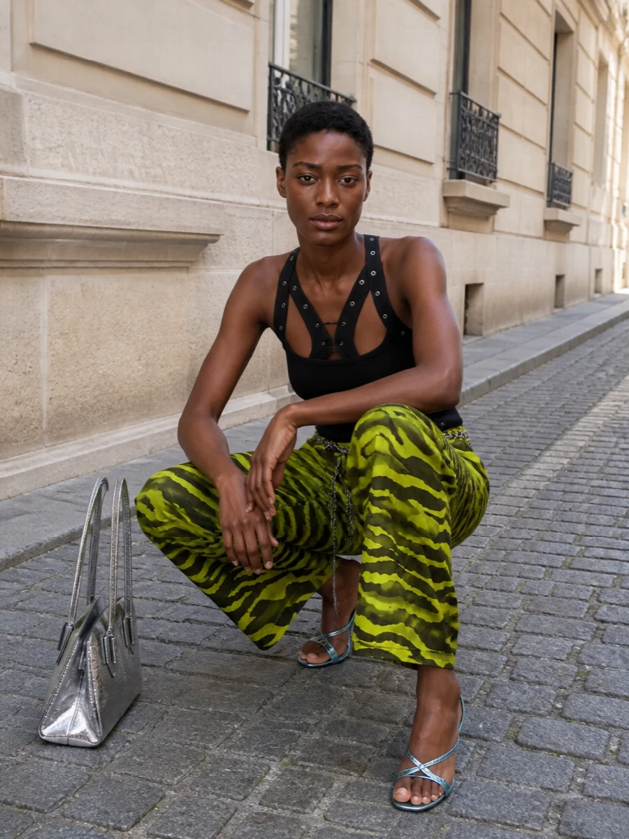 Neon tiger pants go pure Attico after-dark with a black lace‑up tank that sharpens all that print into something graphic and intentional. Cool metallic heels and a mirrored bag keep the story high-glam without more pattern, while a silver chain at the waist pulls everything into a clean, club-ready line.