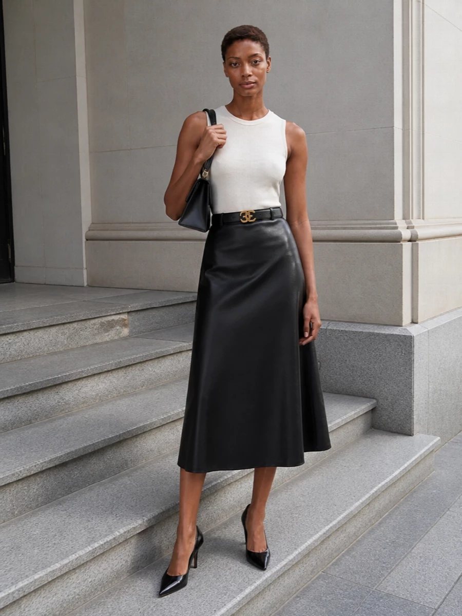 An ivory Balenciaga tank meets a liquid black A-line midi for a clean, elongated silhouette in graphic monochrome. Pointed black pumps and a sculpted black top-handle bag keep the mood quietly assertive. A slim logo belt pulls everything into a single, precise line of modern tailoring.