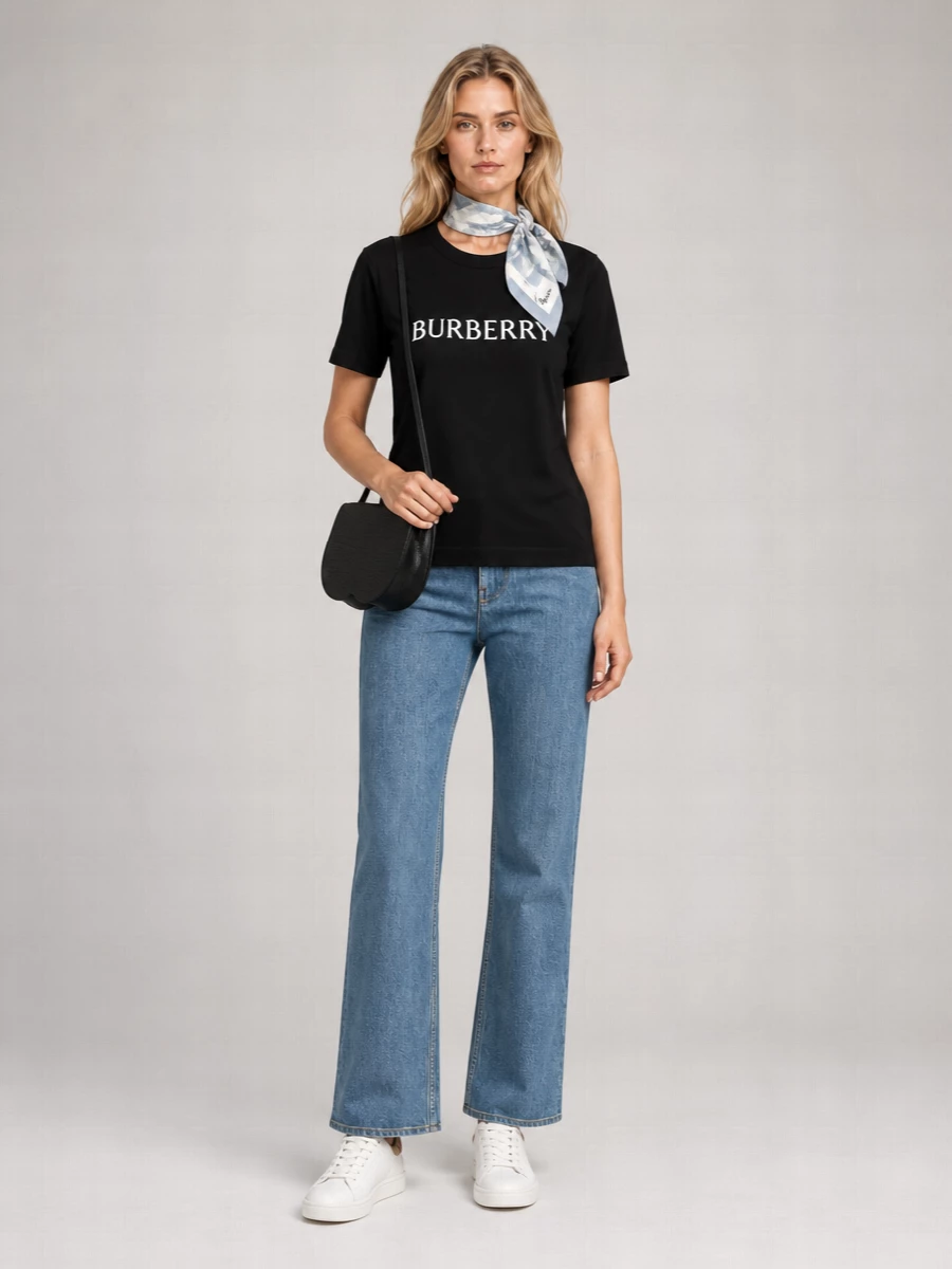 A jet black logo tee and straight blue denim set a clean Burberry uniform that feels relaxed but intentional. White leather sneakers keep everything sharp yet easy, while a sculpted black cross-body and soft watercolor-check scarf add just enough polish. The result is quietly branded city dressing that still feels unfussy and modern.