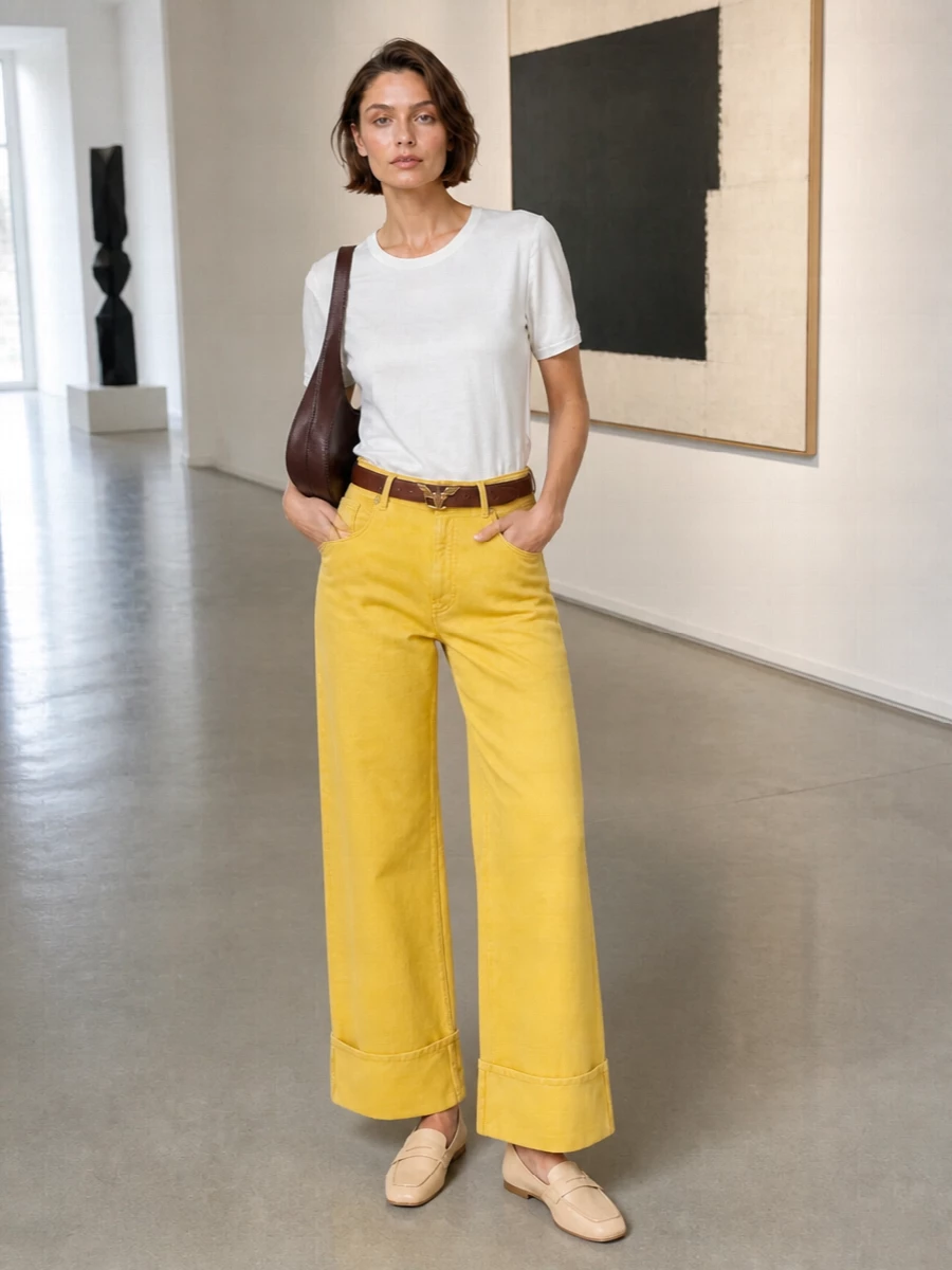Sunny yellow wide legs are cooled off with a clean satin tee for a modern, easy day outfit. Soft butter loafers and a sculptural brown shoulder bag ground the colour with quiet restraint. A slim brown belt finishes the line, keeping the proportions crisp around the mid-rise and wide cuff.