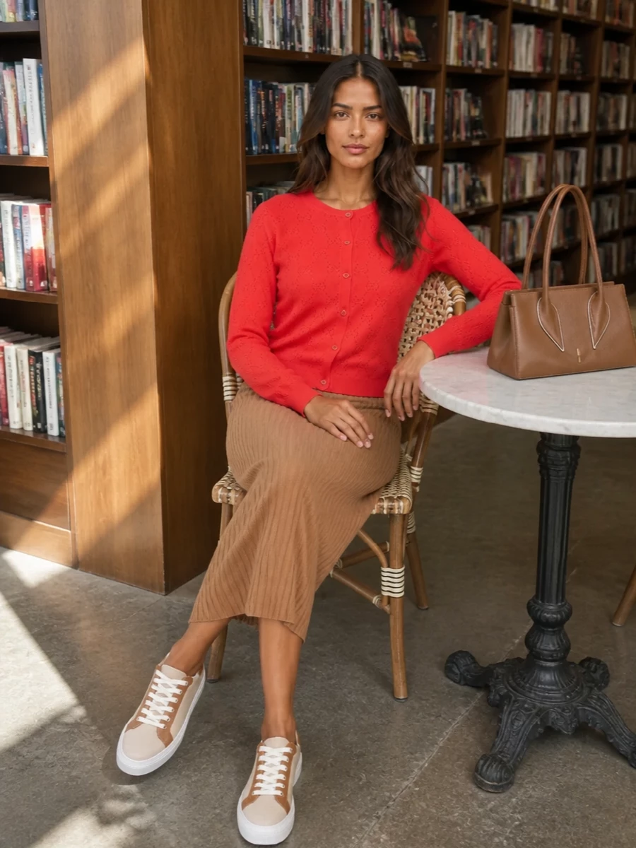 Gucci’s vivid red cardigan is tempered by the softly structured camel ribbed midi, creating a warm, quietly luxurious column of color. Neutral oat sneakers and a caramel top-handle bag keep the mood polished yet relaxed, ideal for refined daytime in the city. The result feels considered and modern, with the red reading as a confident accent rather than a shout.