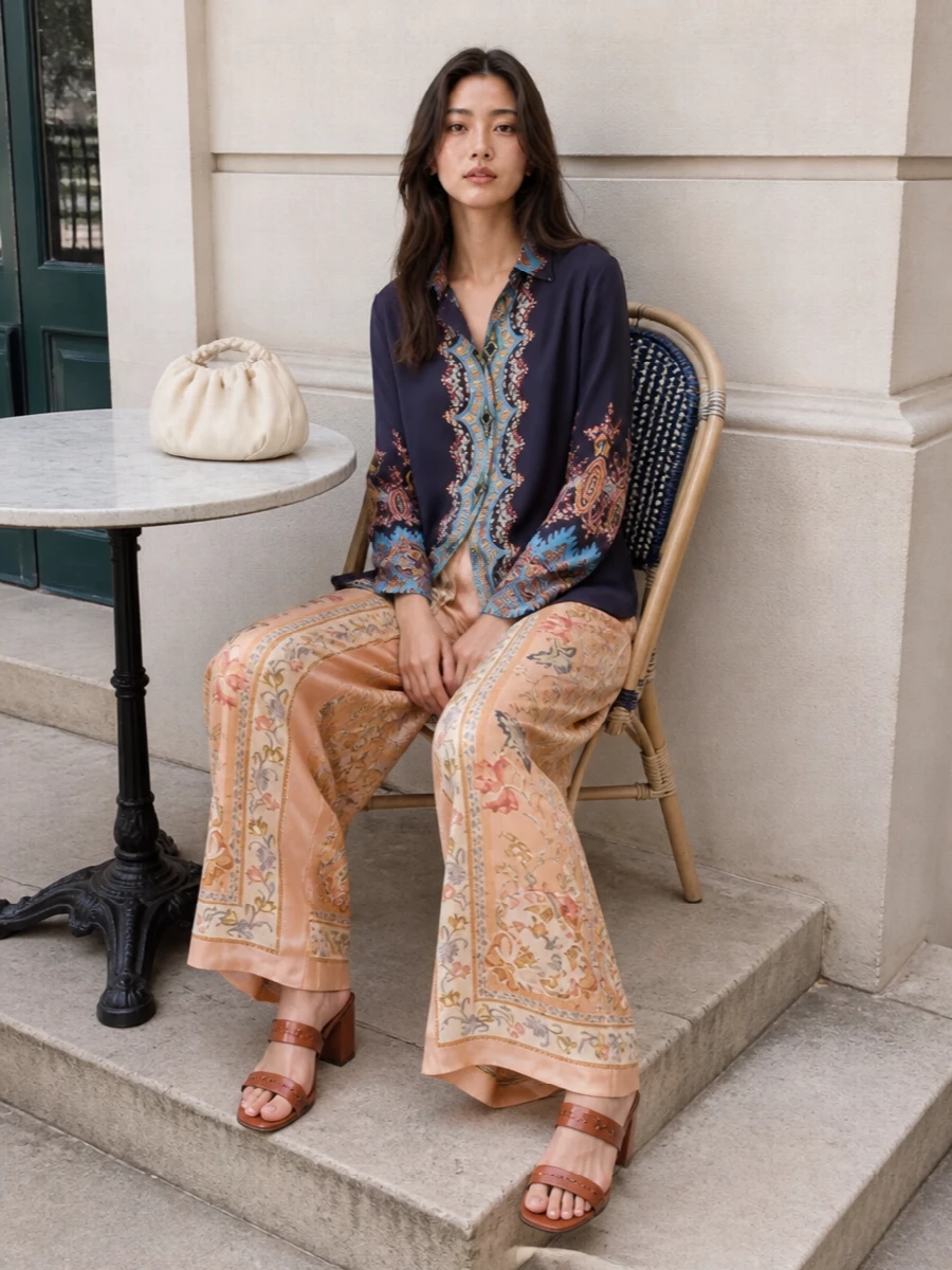 Etro’s long-line paisley shirt pairs with Zimmermann’s scarf-print wide-leg trouser for a richly patterned, boho-romantic ensemble that still reads composed. The shared navy and warm peach tones create a cohesive vertical flow, while the high waist and fluid legs balance the shirt’s length. Terracotta block-heel sandals and a cloud-soft ivory mini bag keep the mood relaxed yet dinner-ready, with texture doing the quiet work of luxury.