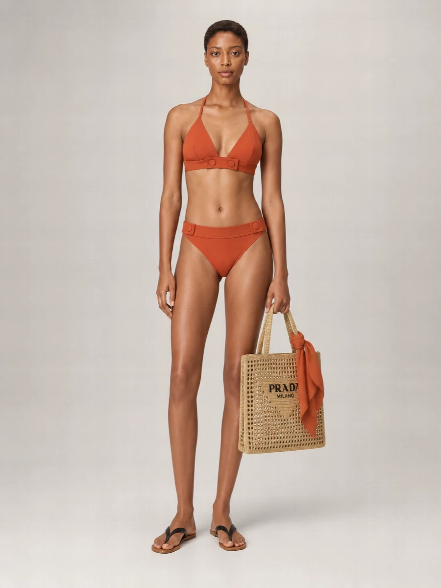 Burnt terracotta swim paired with the matching high-cut brief creates a lean, quietly glamorous line that still feels easy on the sand. Ultra-flat black leather sandals and a sand-toned crochet tote keep the mood minimal and resort ready. A sheer terracotta scarf threads the color through again, whether tied at the neck or looped through the bag handle for a subtle, curated finish.