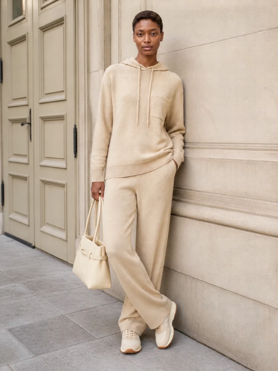 A fully tonal knit pairing keeps everything soft and calm, with warm beige running from hoodie to lounge pant. Layered textures and subtle logo touches make it feel considered rather than casual-only. Neutral sneakers and a structured buttercream bag bring just enough city polish while staying in that serene, off-duty space.