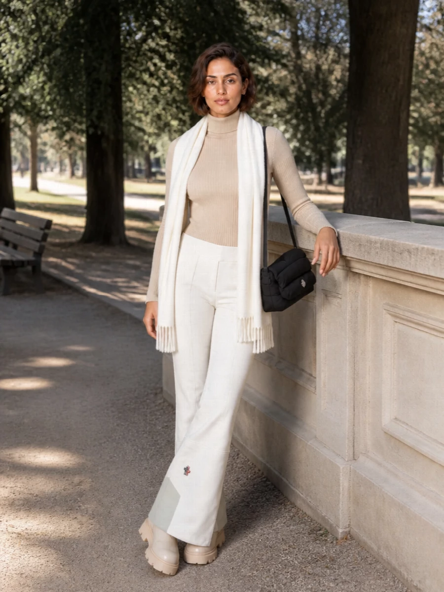 Moncler’s off-white flared ski pant is paired with a slim beige mock-neck knit for a clean, body-hugging base that feels quietly technical rather than overtly sporty. Chunky shearling ankle boots echo the winter neutrals and add just enough weight under the flared hem. A padded black shoulder bag and winter-white scarf complete a monochrome alpine palette that moves easily from lift to lounge with minimal fuss and maximum polish.