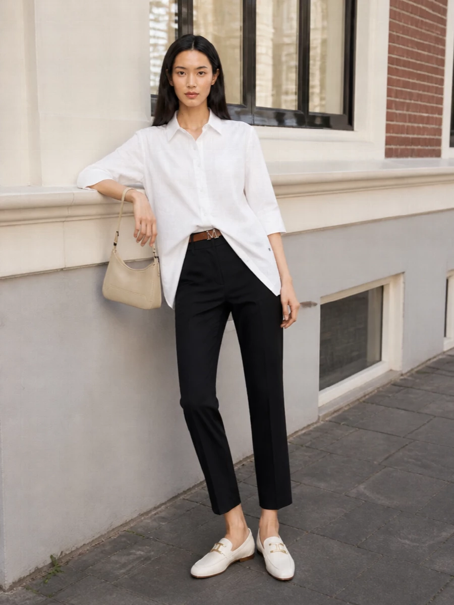 A relaxed white longline shirt meets sharp ink navy tailoring for a clean, minimalist column that works from desk to dinner. Ivory loafers and a butter-cream baguette keep the palette soft and refined, while a slim tan belt quietly defines the waist without disturbing the ease of the silhouette. The result is modern, understated polish with just enough structure to feel considered but never stiff.