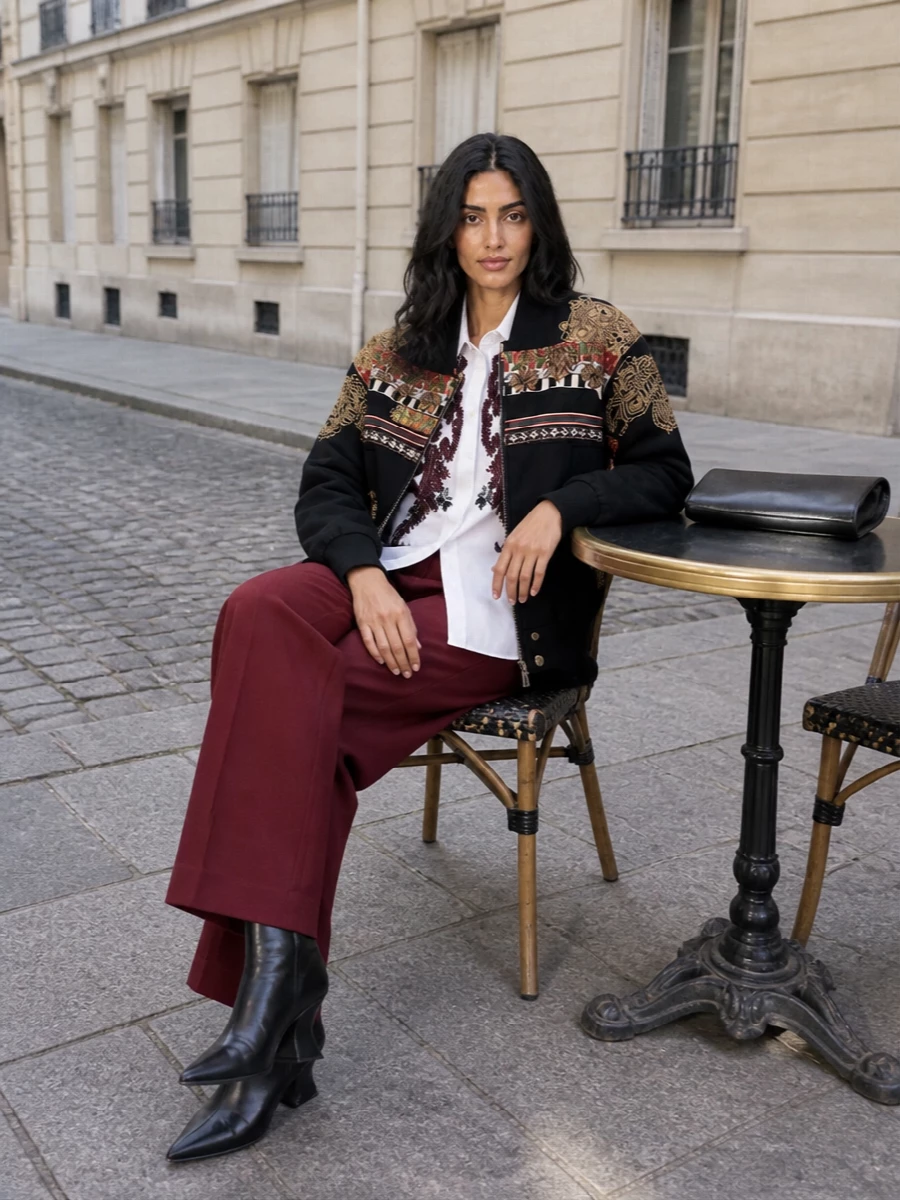 This is the Dries bomber at its most convincing: anchored by deep burgundy tailoring and a crisp, embroidered shirt that quietly echoes its folkloric detail. The sculpted black wedge boots and glossy frame clutch sharpen the volume, keeping the drama intelligent rather than costume. I chose tailoring over a dress so the bomber remains the clear hero, with proportion and palette pulled into a long, graphic column under all that embroidery.