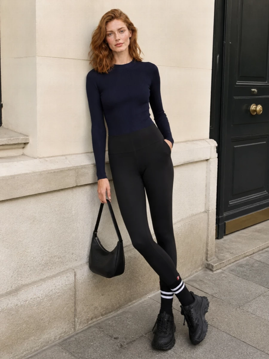 This look builds a sharp, athletic column around the Moncler Grenoble track pants, pairing them with a navy ribbed top for a sleek, body-skimming silhouette that still feels effortless. Chunky black sneakers and a curved black hobo bag keep the mood polished yet pragmatic, while striped socks add a discreet graphic accent that nods to sport and prep without overwhelming the minimalism.