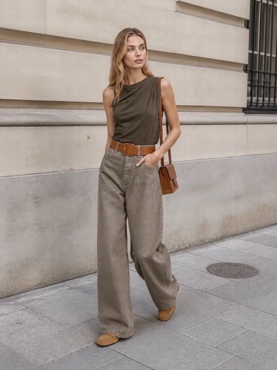 This look leans into sun-soft neutrals with an earthy, architectural twist: the high-rise taupe wide-leg trouser is anchored by a draped olive-brown sleeveless top that keeps the upper body clean and elongating. Camel suede loafers and a slim tan-stitched shoulder bag continue the warm palette, while a structured tan belt neatly cinches the waist for a quietly polished, gallery-to-dinner-ready silhouette.
