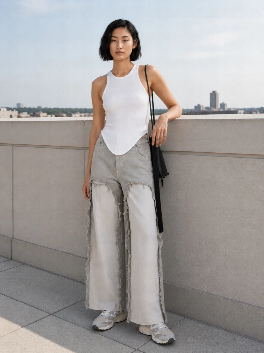 Soft neutrals and sharp lines keep the deconstructed trouser feeling intentional, with the Drkshdw tank tracing the same asymmetric geometry in a clean white. Cushioned New Balance sneakers pull the look toward grounded streetwear, while the slim black cross-body adds just enough structure and contrast for city days. The result is directional but genuinely wearable, built for movement and long hours out.