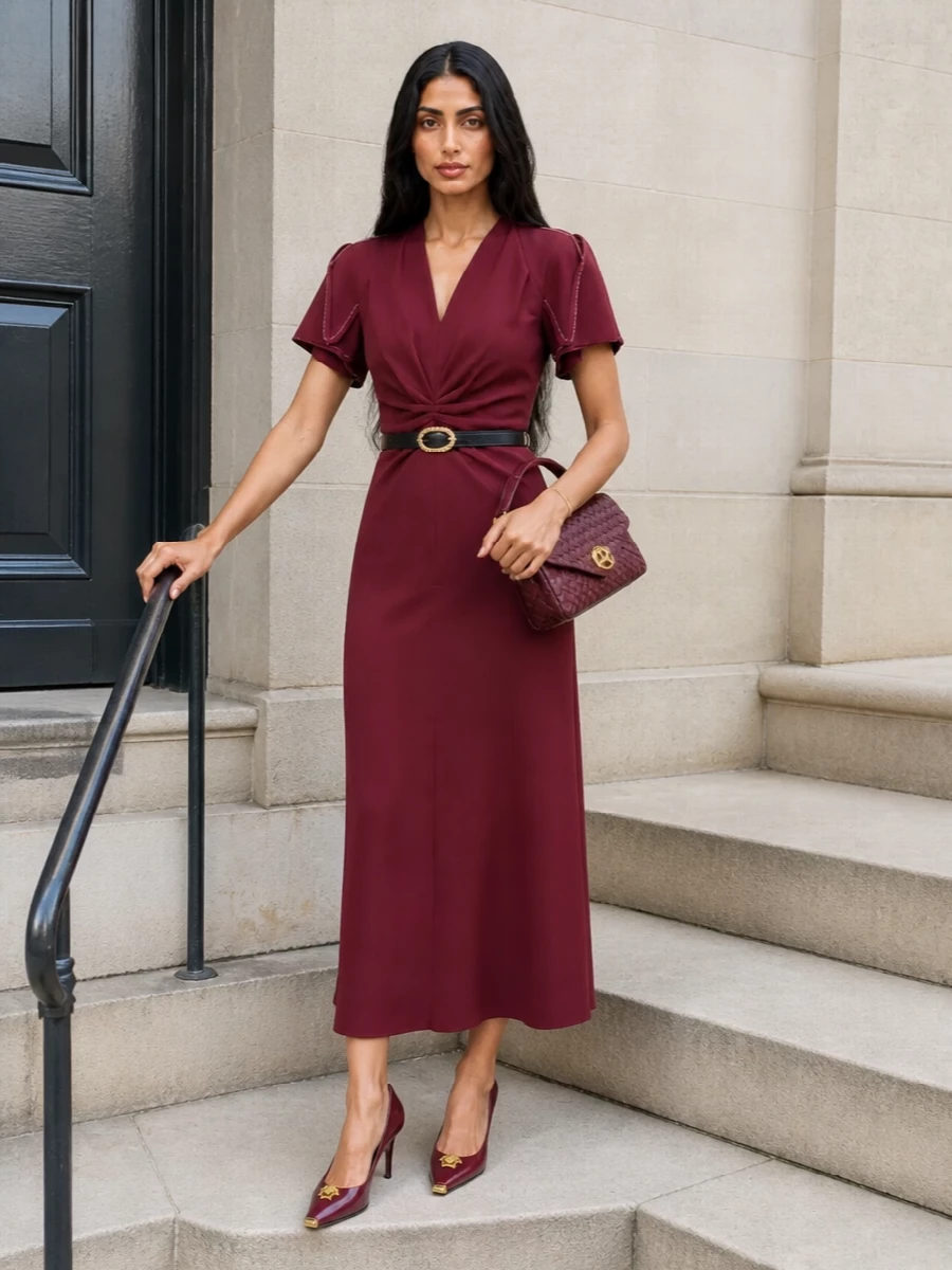 A deep burgundy column anchors this evening ensemble, its precise ruching and V-neck framed by tonal heels and a woven leather shoulder bag in the same wine-rich hue. Gold hardware and a slim crystal-detailed belt introduce a controlled shimmer, keeping the mood sculpted and intimate rather than overtly showy. It is a quietly assertive cocktail combination that feels as considered from a gallery opening as it does at a late restaurant table.